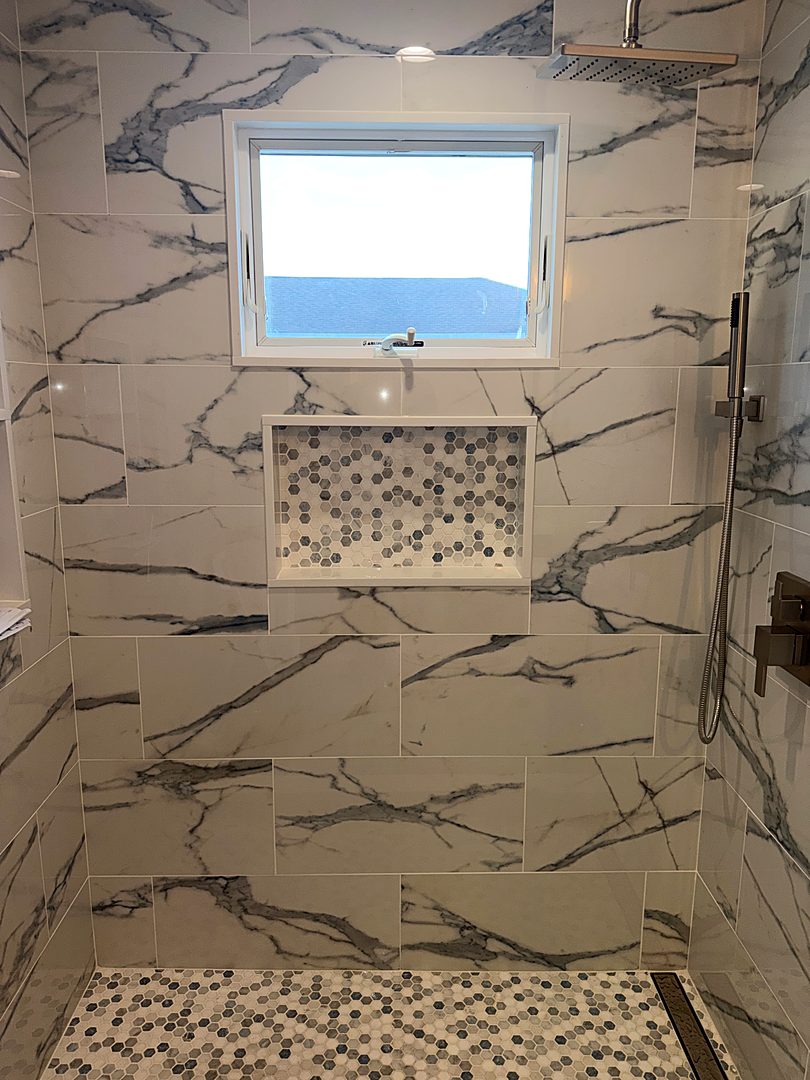 Finished shower with large marble-look tile, a mosaic niche, and a pebble floor