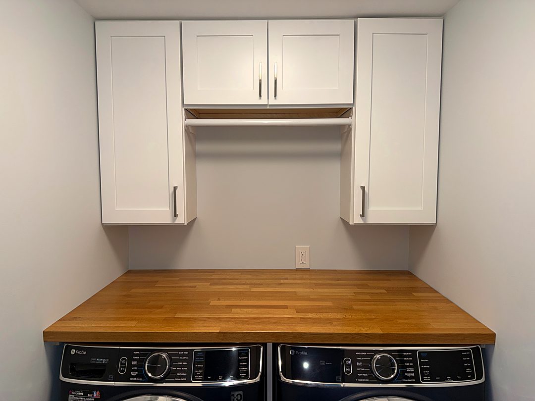 Laundry nook with white upper cabinets and a butcher block counter over the washer and dryer