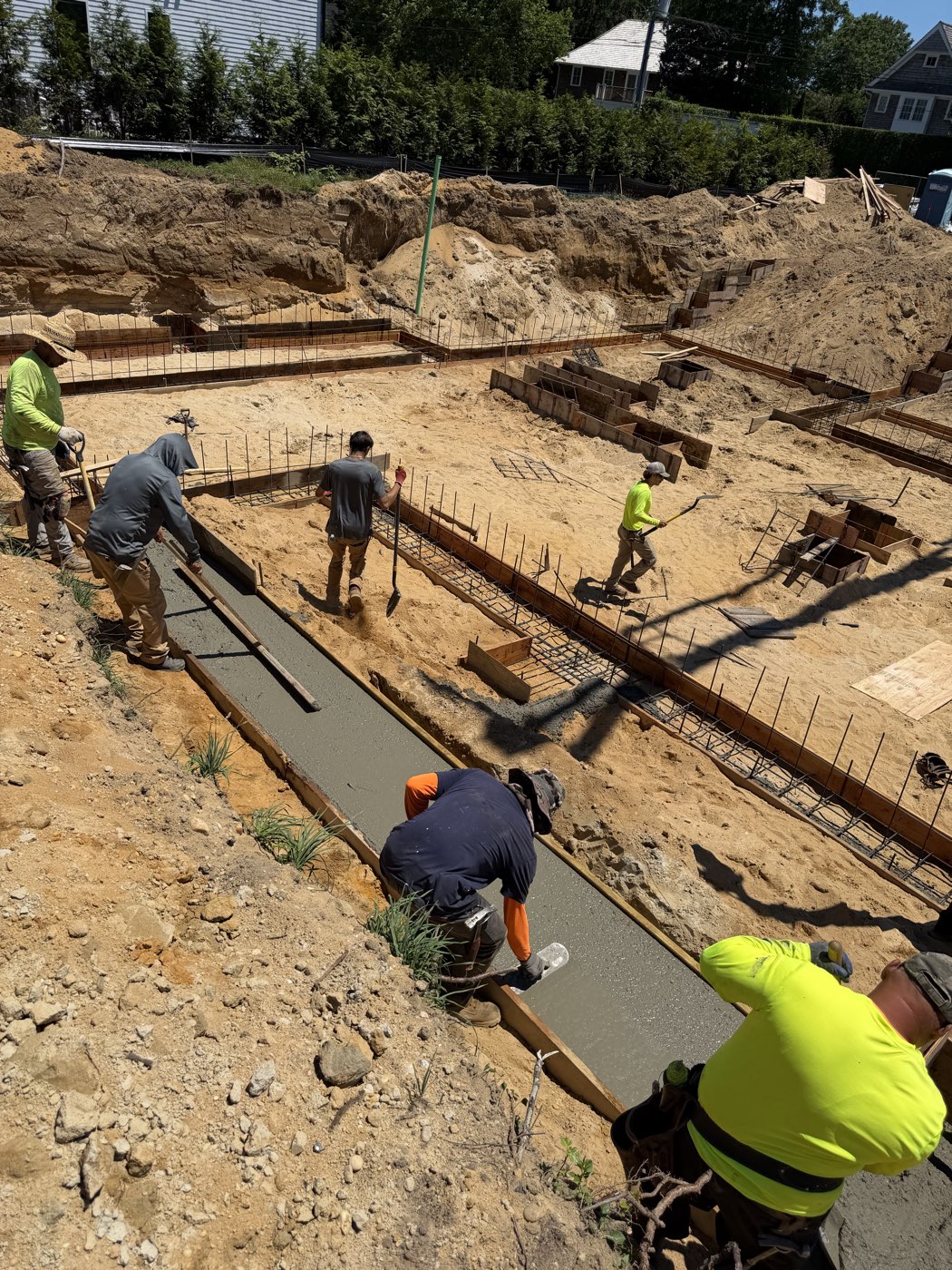 Crew screeding wet concrete along the footing trench on pour day at the custom home site