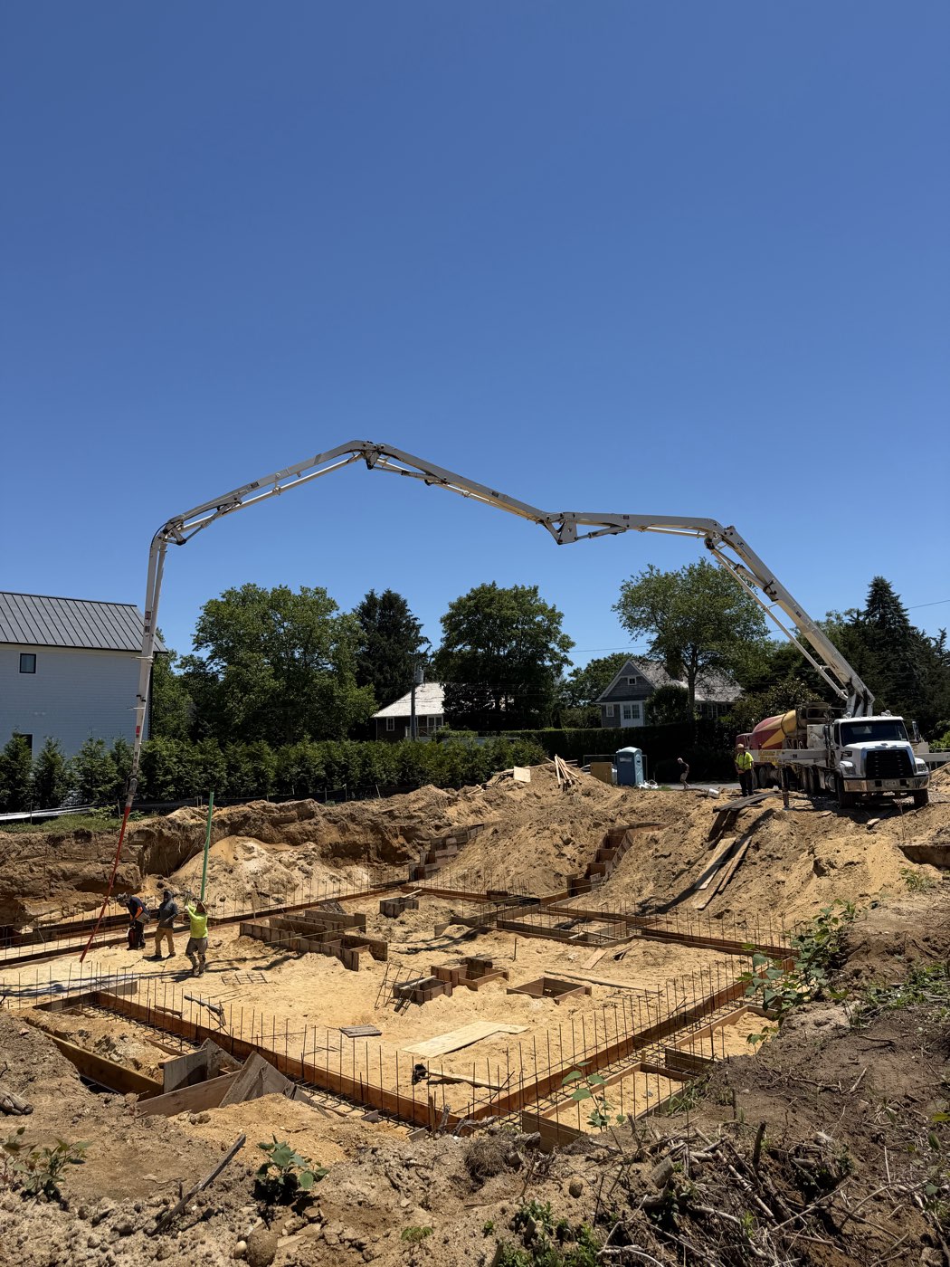 Concrete pump truck set up at the street with its boom reaching over the excavated site