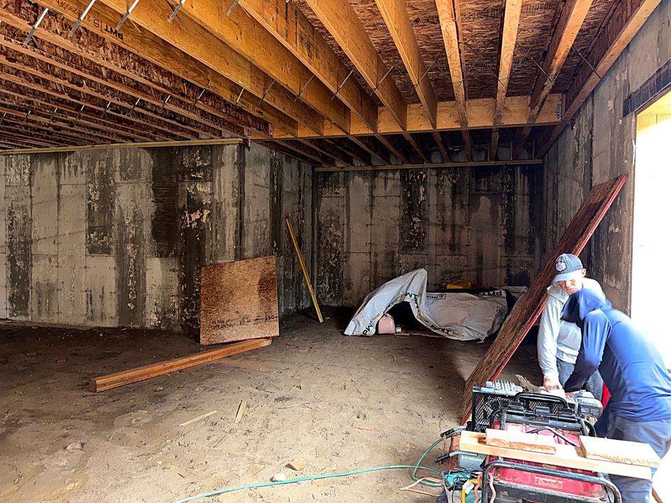 Crew cutting lumber in the basement beneath the new floor framing