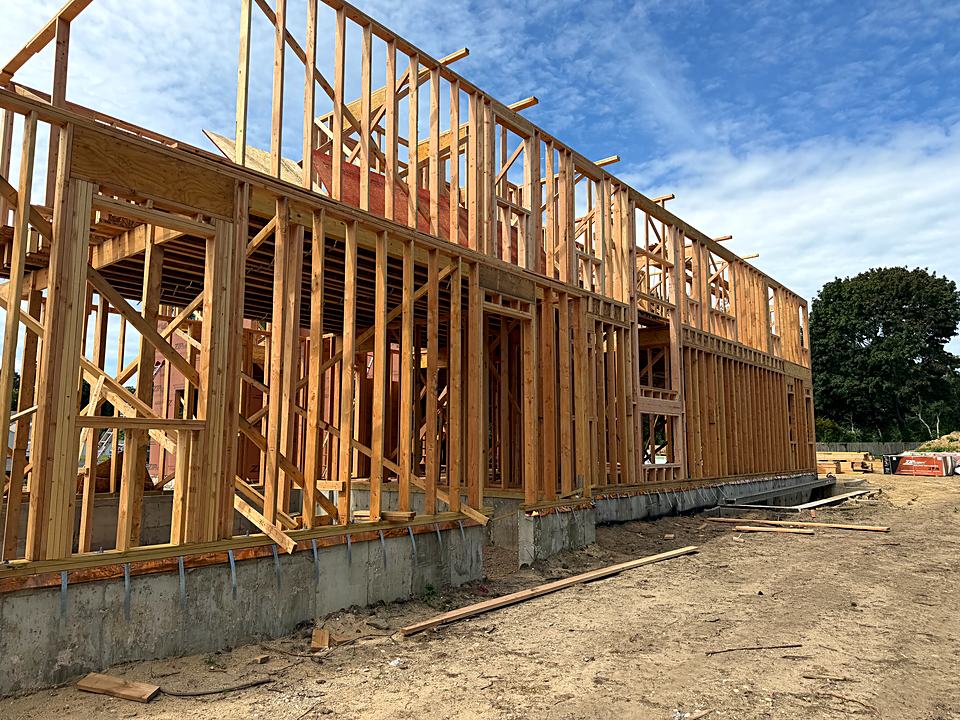 Tall exterior wall framing rising above the foundation against a blue sky