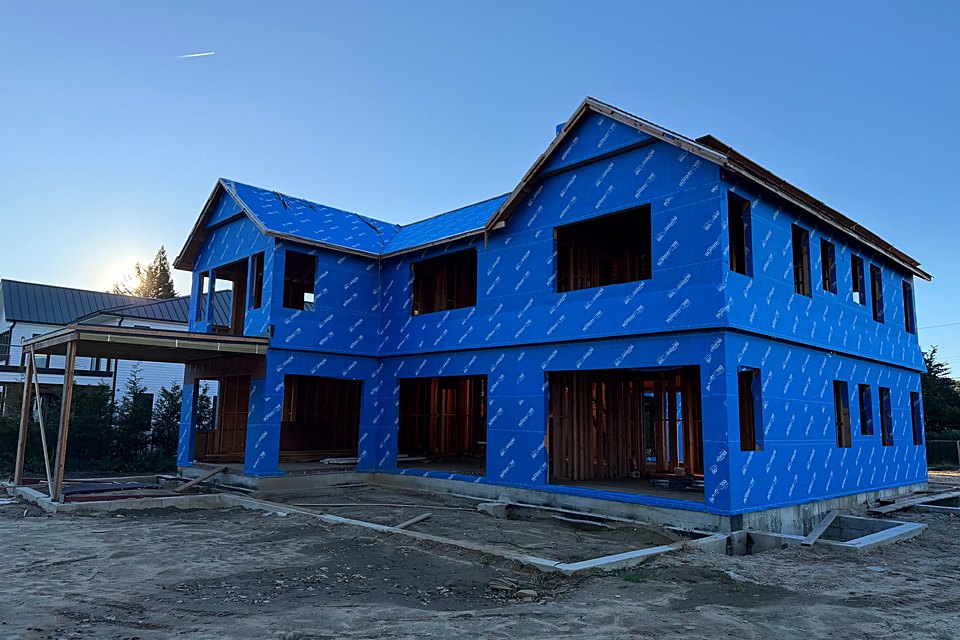 The two-story custom home wrapped in blue house wrap, seen from the side