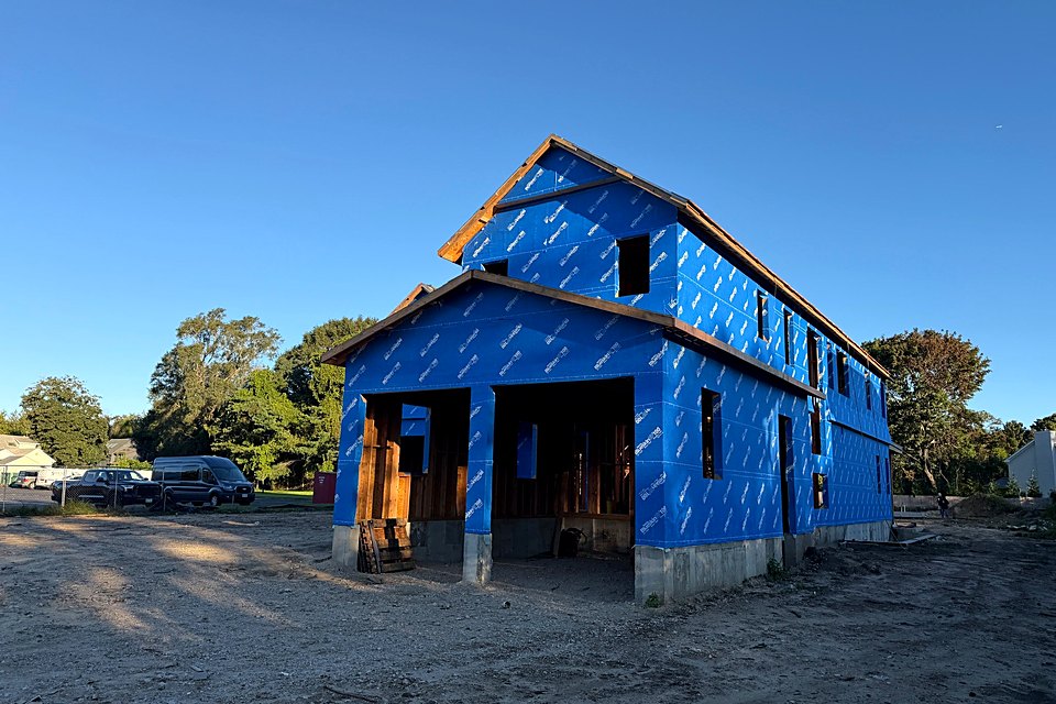 Front of the custom home in house wrap with the garage openings framed