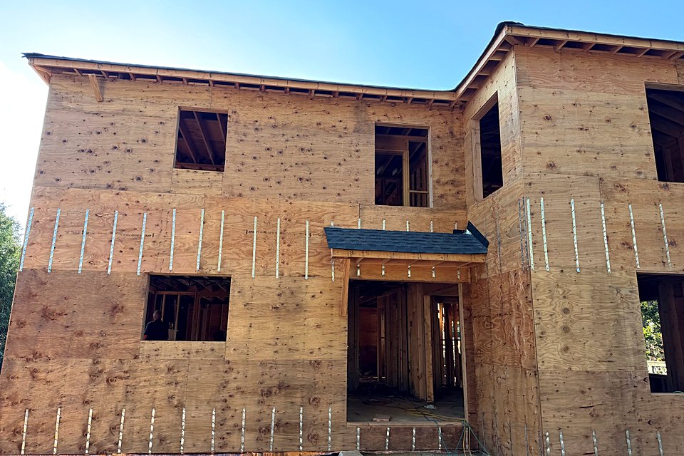Two-story custom home sheathed in plywood with the entry overhang framed