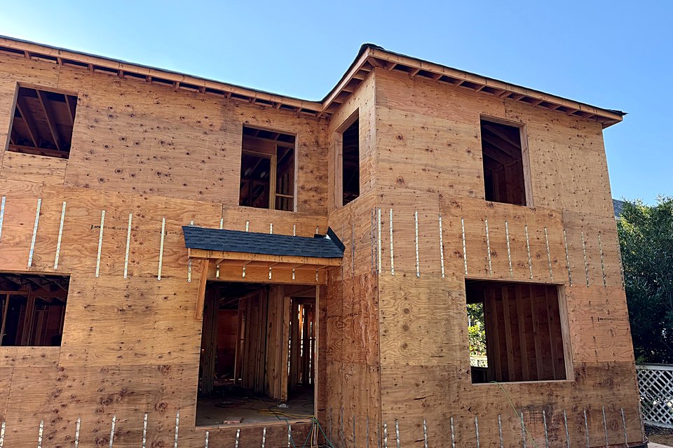 Corner of the custom home sheathed in plywood with metal straps across the seams