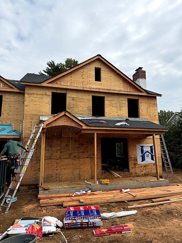 Crew member climbing a ladder at the front of the sheathed custom home