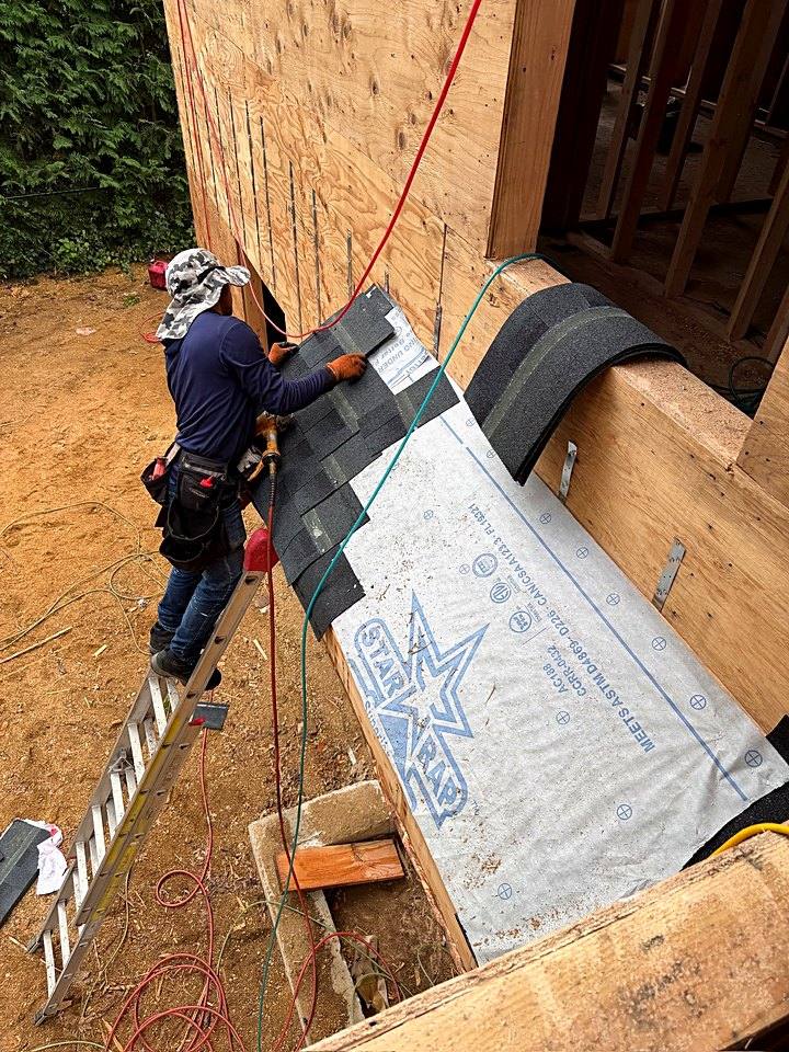 Crew member nailing architectural shingles over underlayment on a lower roof