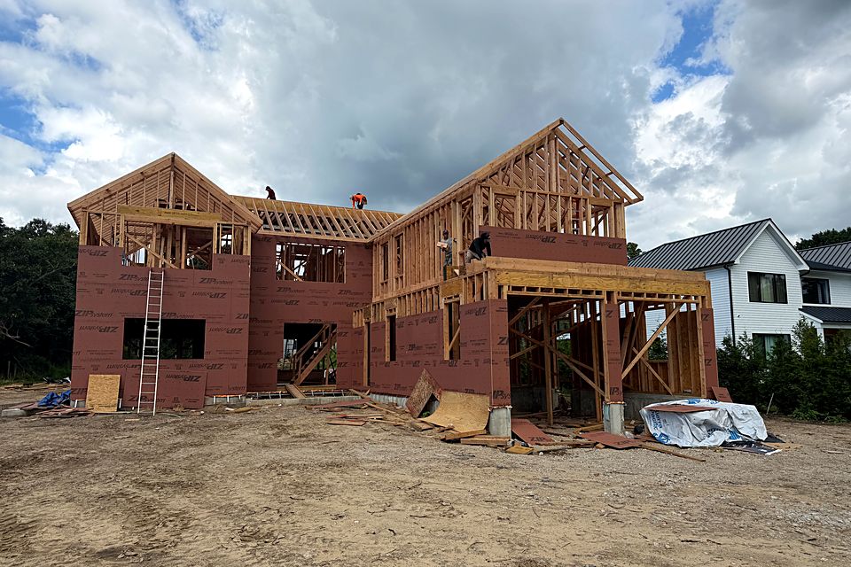 Two-story custom home in the framing stage, with the roof gables framed, the walls sheathed, and the crew working up top