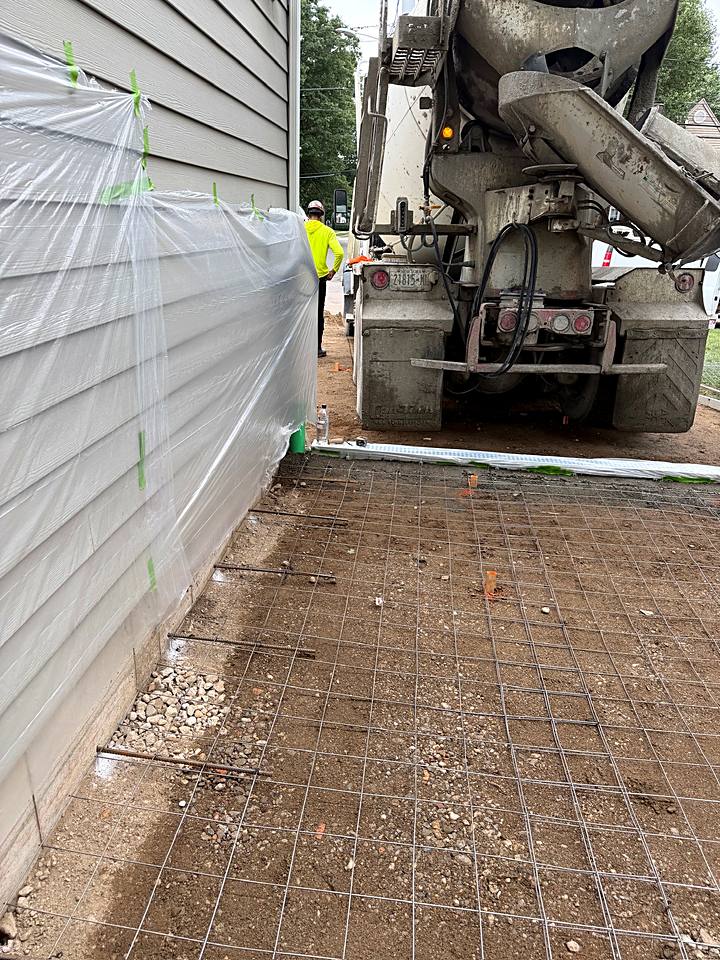 Concrete truck pouring over wire mesh along the side of the house