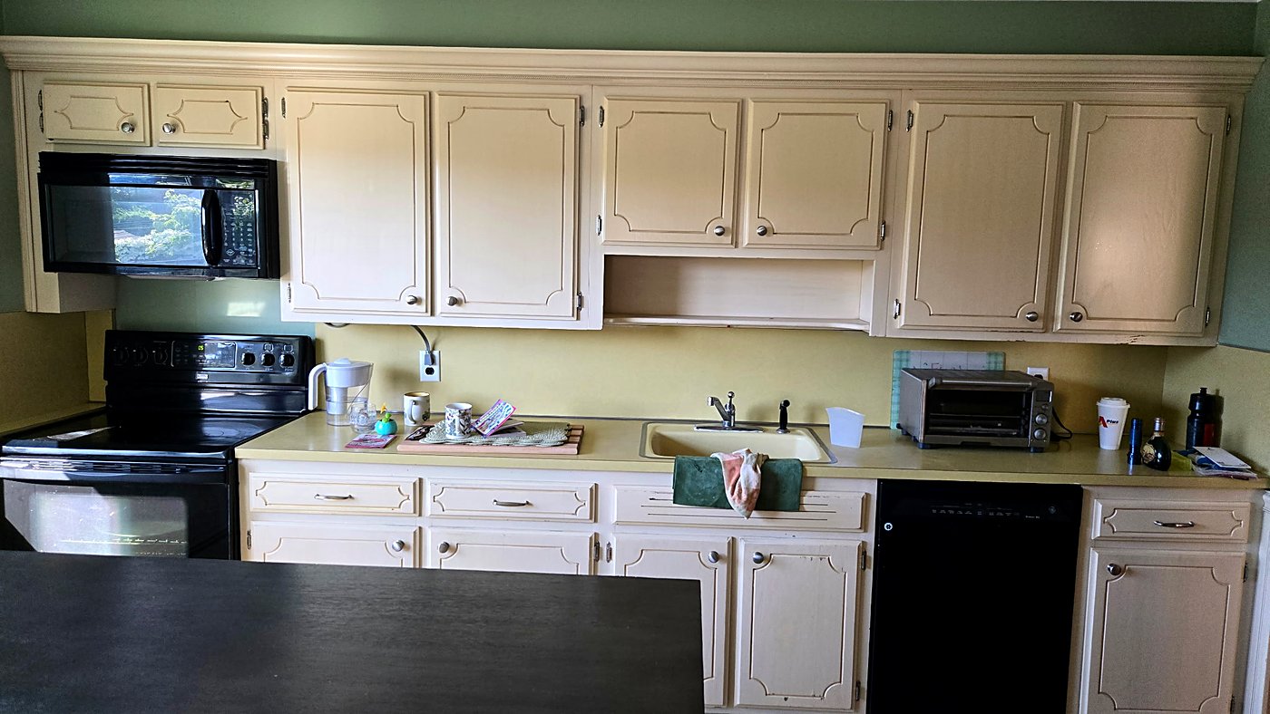 Dated kitchen with cream cabinets and a black range before the remodel