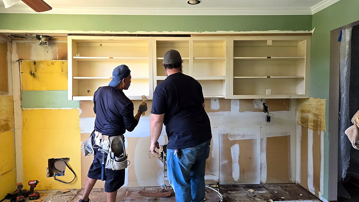 Two crew members removing the old kitchen cabinets