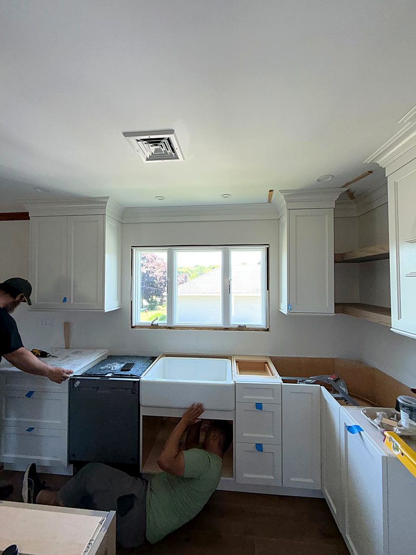 Installer working under the sink base while the new white cabinets are set