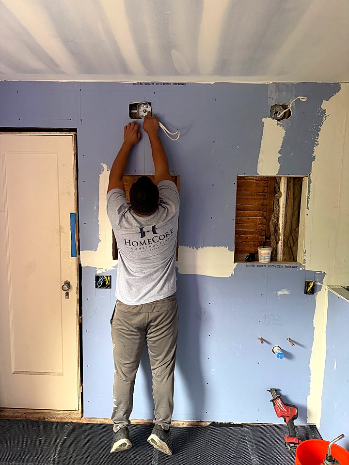 Crew member in a HomeCore shirt prepping the wall above the doorway