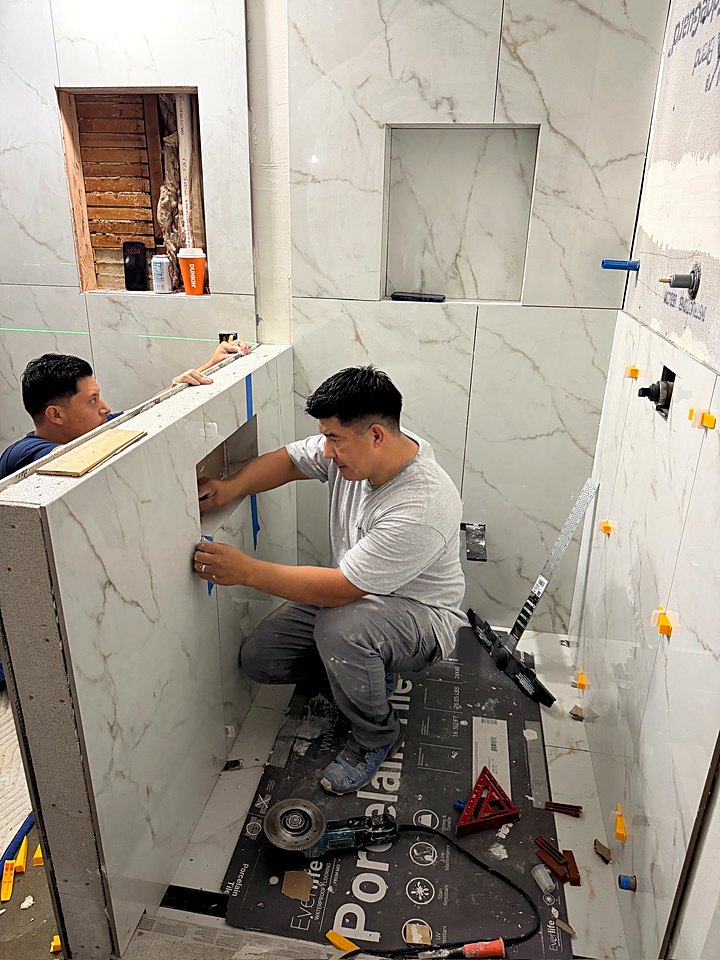 Two crew members tiling the shower curb and walls