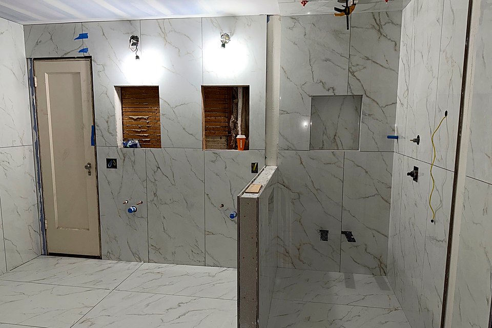Bathroom tiled floor to ceiling with twin niches and a half wall at the shower
