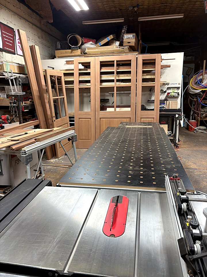 Table saw in the shop with a glass-paneled door unit in progress behind it