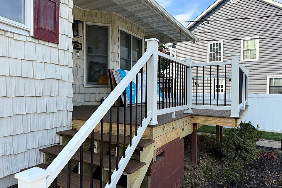 New composite porch stairs and a white railing with black balusters installed, with the trim still to come
