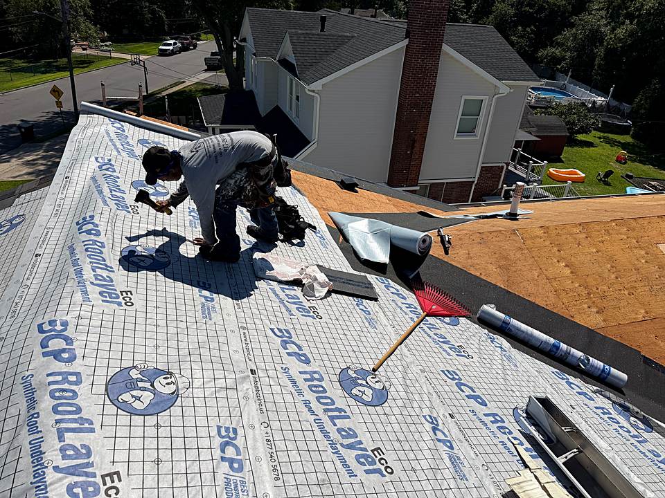 Roofer installing synthetic underlayment on the roof deck