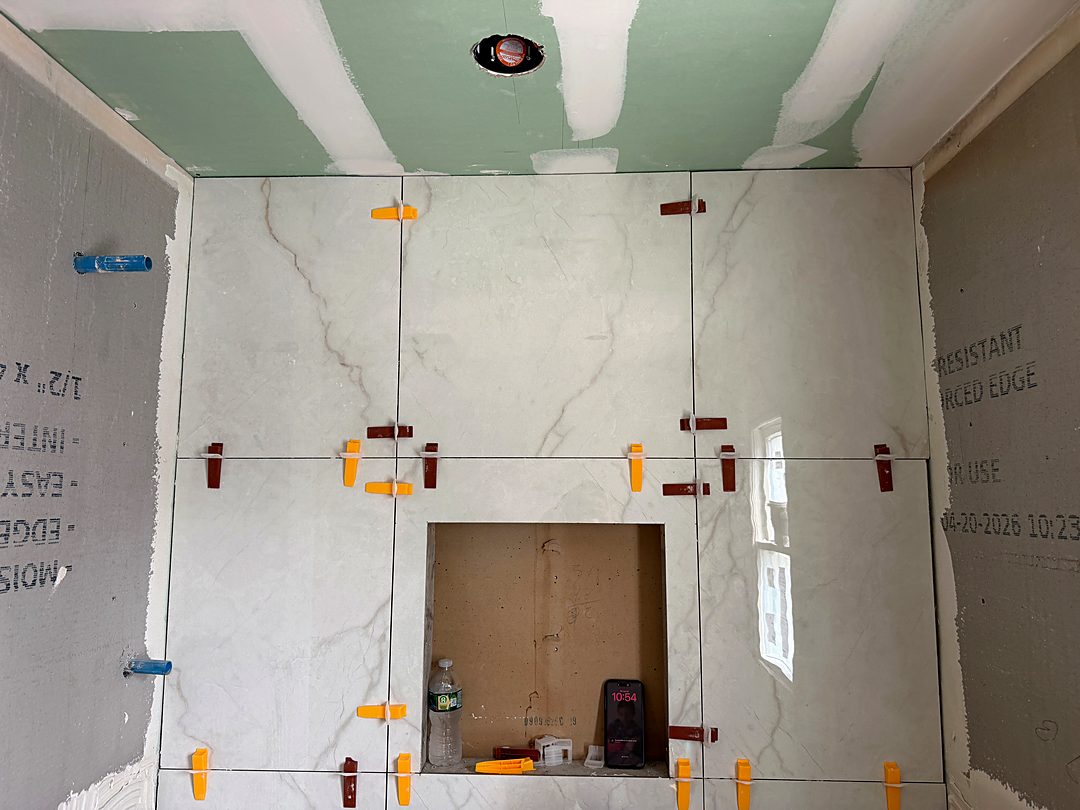 Large marble-look tile going up in a shower with leveling clips around the niche
