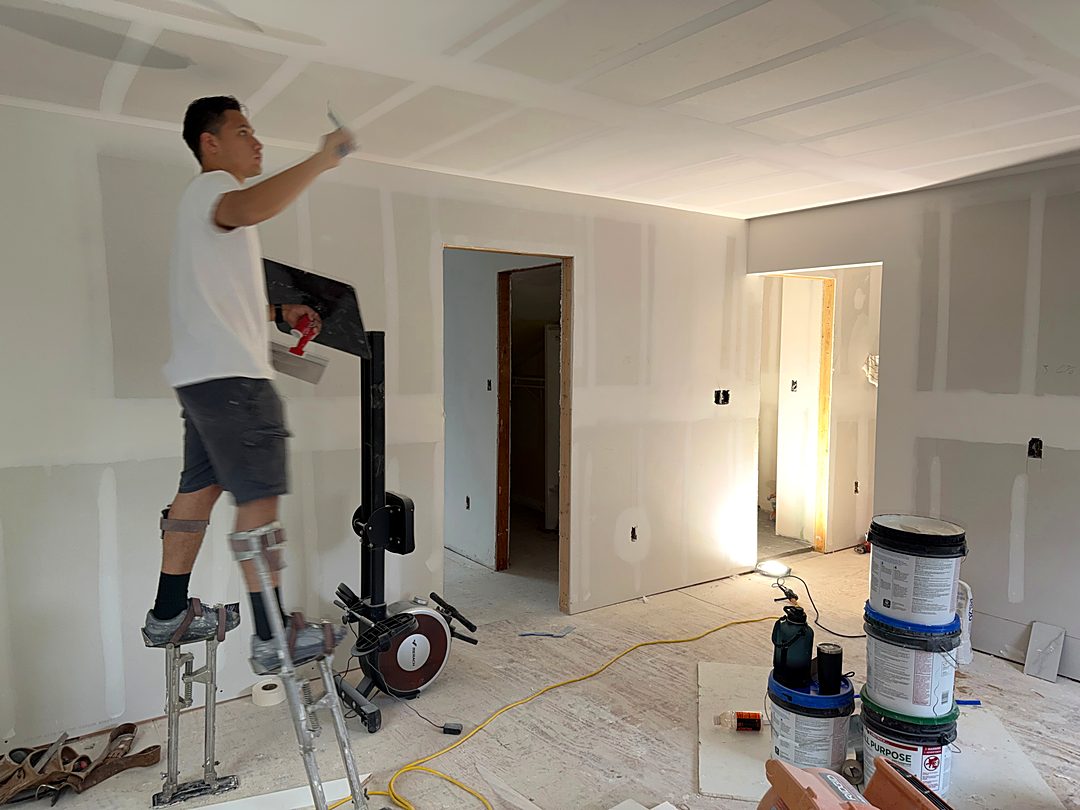Drywall finisher on stilts taping the ceiling of a renovated room