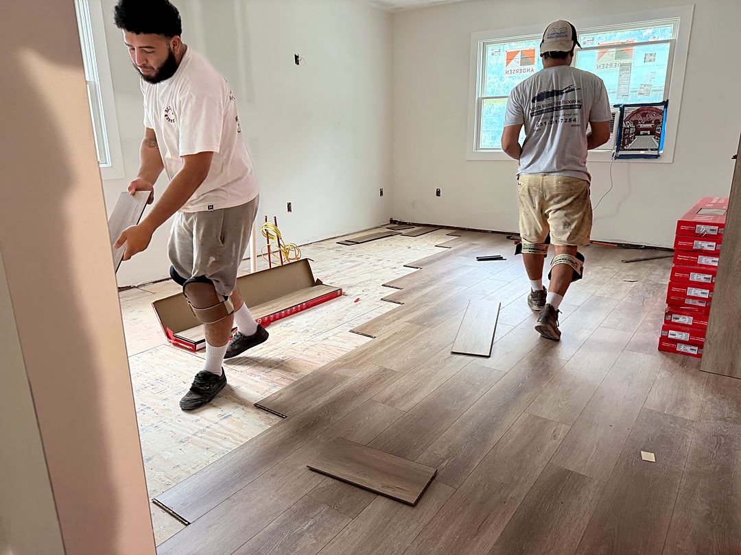 Two installers laying new plank flooring in a bedroom