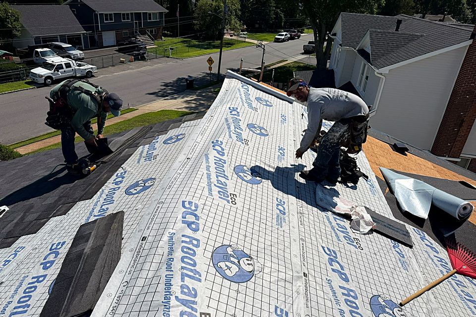 Two roofers laying new underlayment across the roof deck