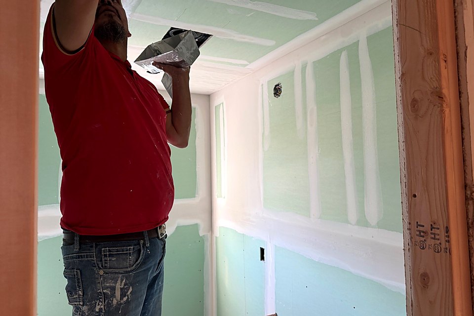 Finisher taping new drywall seams in a bedroom