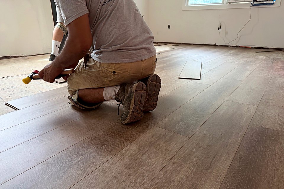 Installer fitting new plank flooring along the wall