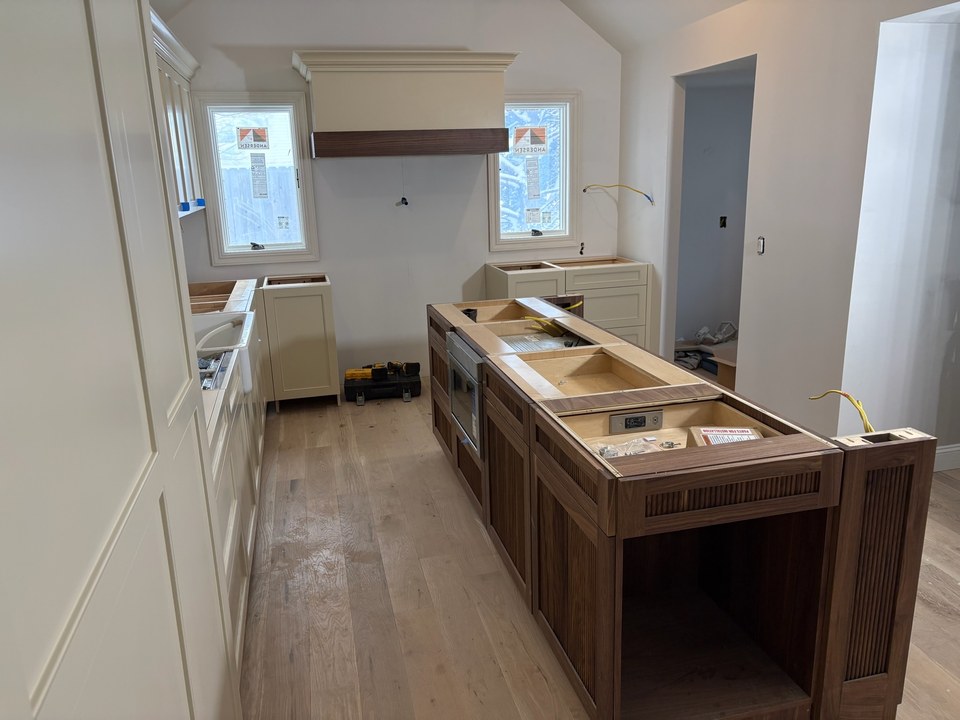 Custom walnut island with fluted panels being installed beside painted inset cabinetry