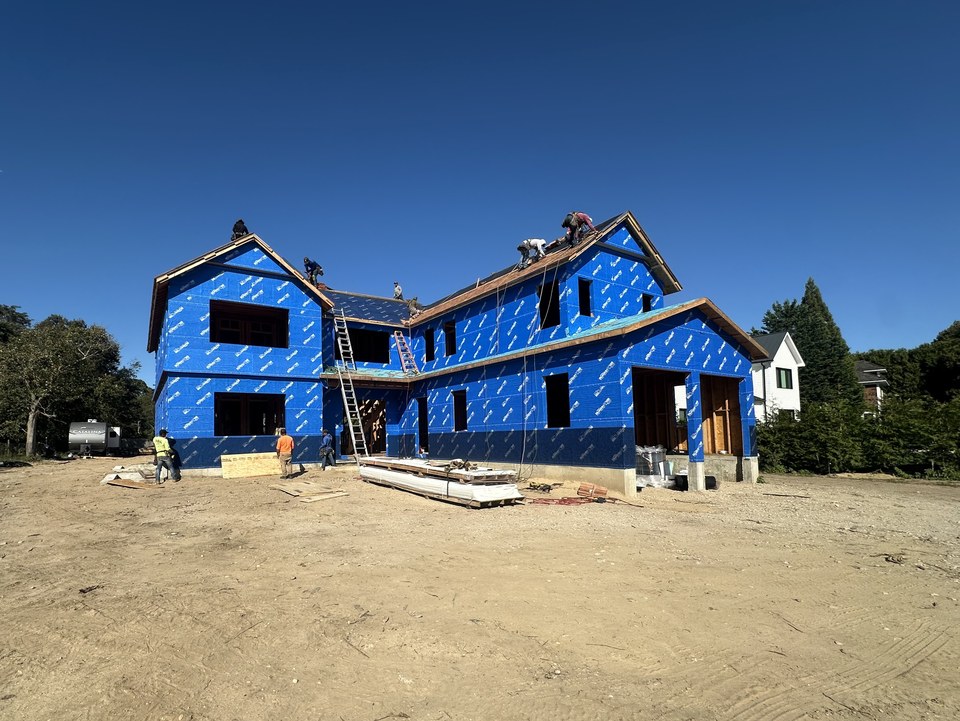 HomeCore crew framing and roofing a new two-story custom home wrapped in blue house wrap
