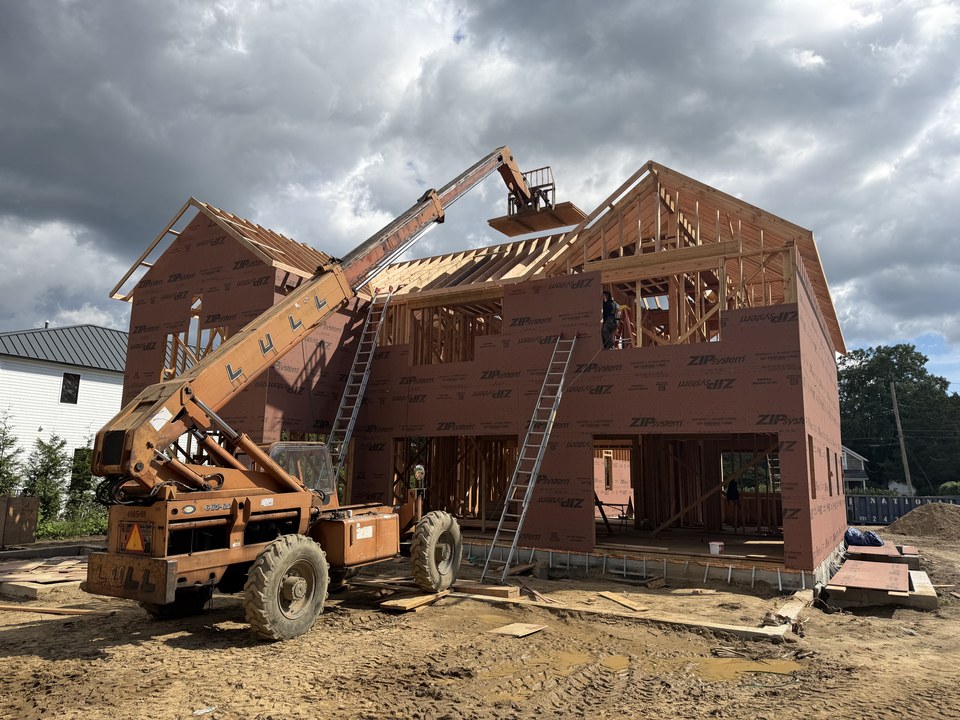 New two-story home sheathed in ZIP System panels with the roof framing going up and a lift on site